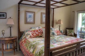 Una cama con dosel con ropa de cama floral, una mesita de noche de madera con lámpara y cuadros enmarcados en la pared.