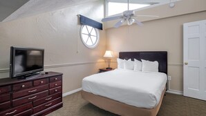 Une chambre d’hôtel avec un lit, un téléviseur posé sur une commode, un ventilateur de plafond, une fenêtre et une porte.