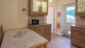 A compact kitchen with wooden cabinets, a microwave, and a dining table set with a placemat. - 2 bedroom accommodation in Oswestry (Oswestry)