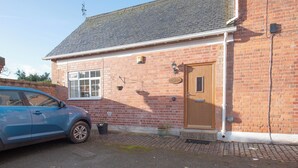 A brick building with a wooden door, a window, and a small garden area with potted plants. - 2 bedroom accommodation in Oswestry (Oswestry)