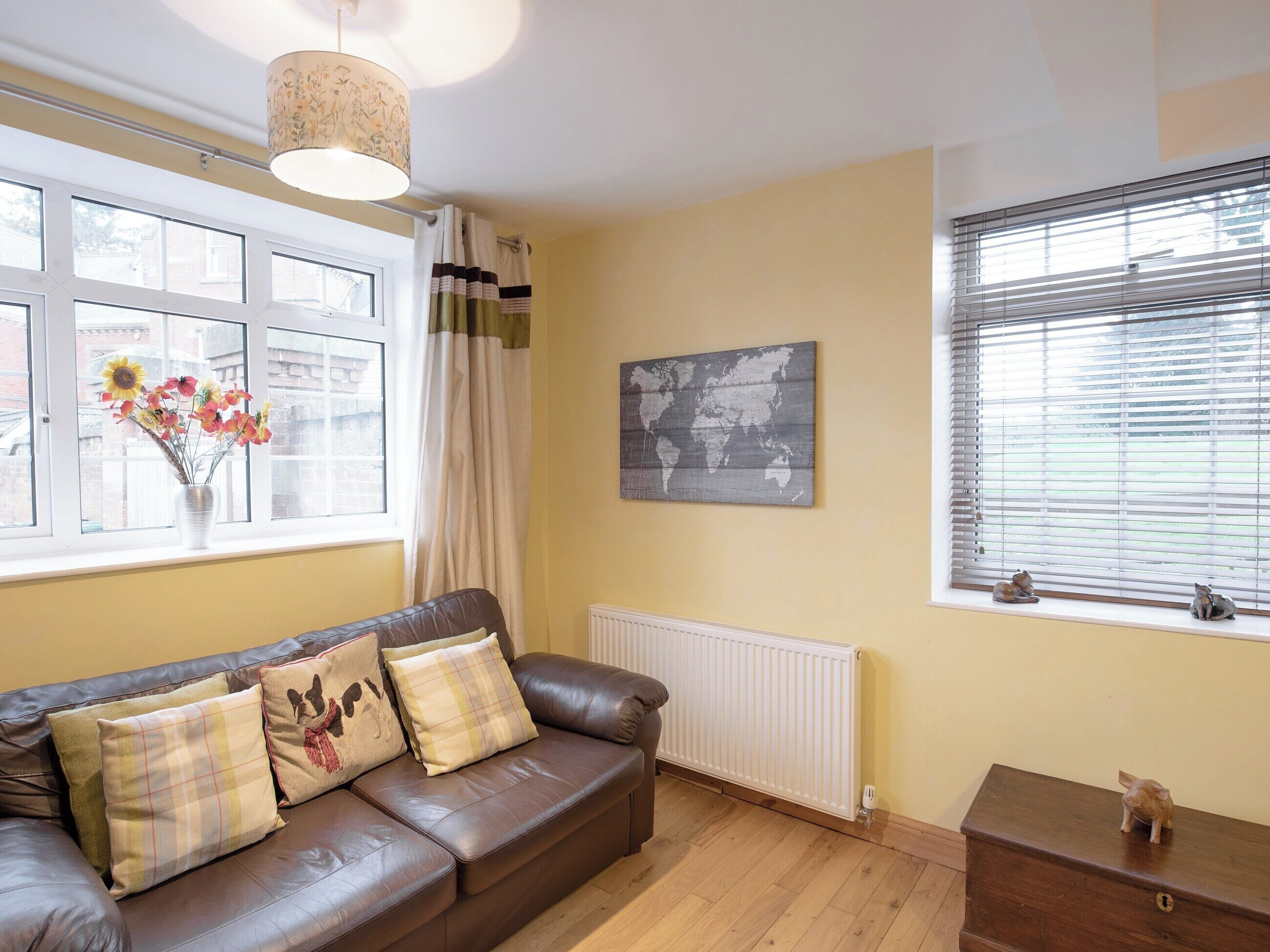 A living room with a brown leather sofa, a world map on the wall, and a window with blinds.