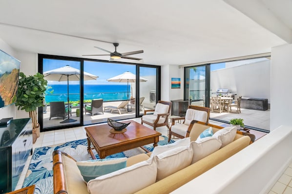 A spacious living area with a large window overlooking the ocean, furnished with a sofa, chairs, and a coffee table.