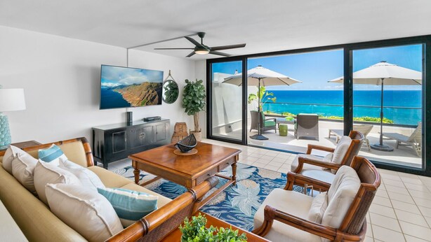 Een ruime woonkamer met een grote televisie, comfortabele zithoek en een balkon met uitzicht op zee.