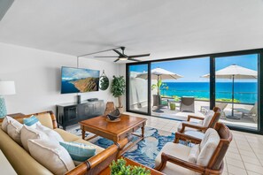 A spacious living room with a large TV, comfortable seating, and a balcony with ocean views.