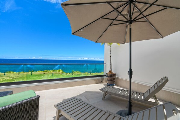 A balcony with a view of the ocean, a potted plant, and two lounge chairs.