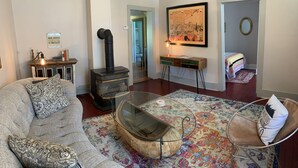 Un salon comprenant un canapé, une table basse en verre, une table d’appoint en bois, un tableau, un fauteuil et une cheminée.