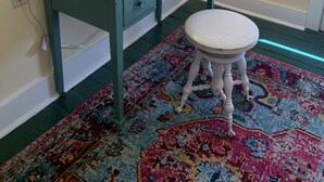 Une pièce comprenant un bureau de couleur turquoise, un petit tabouret, un tapis à motifs, une lampe et un miroir décoratif.