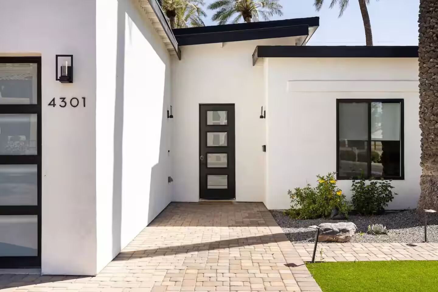 Een modern huis met het nummer 4301 op de deur, een deur met een zwart frame, en een kleine tuin met planten en een rots.