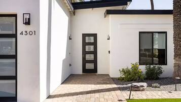 Een modern huis met het nummer 4301 op de deur, een deur met een zwart frame, en een kleine tuin met planten en een rots.