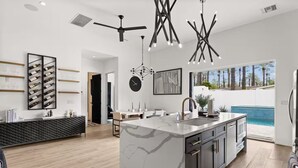 Une cuisine moderne dotée d’un îlot en marbre, de luminaires suspendus et offrant une vue sur une piscine.