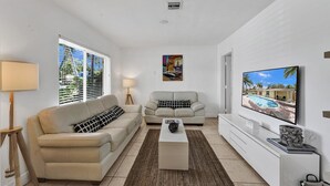 Ein modernes Wohnzimmer mit einem beigen Sofa, einem zusätzlichen Sofa, einem Couchtisch, einem Fernseher und einem Gemälde an der Wand.