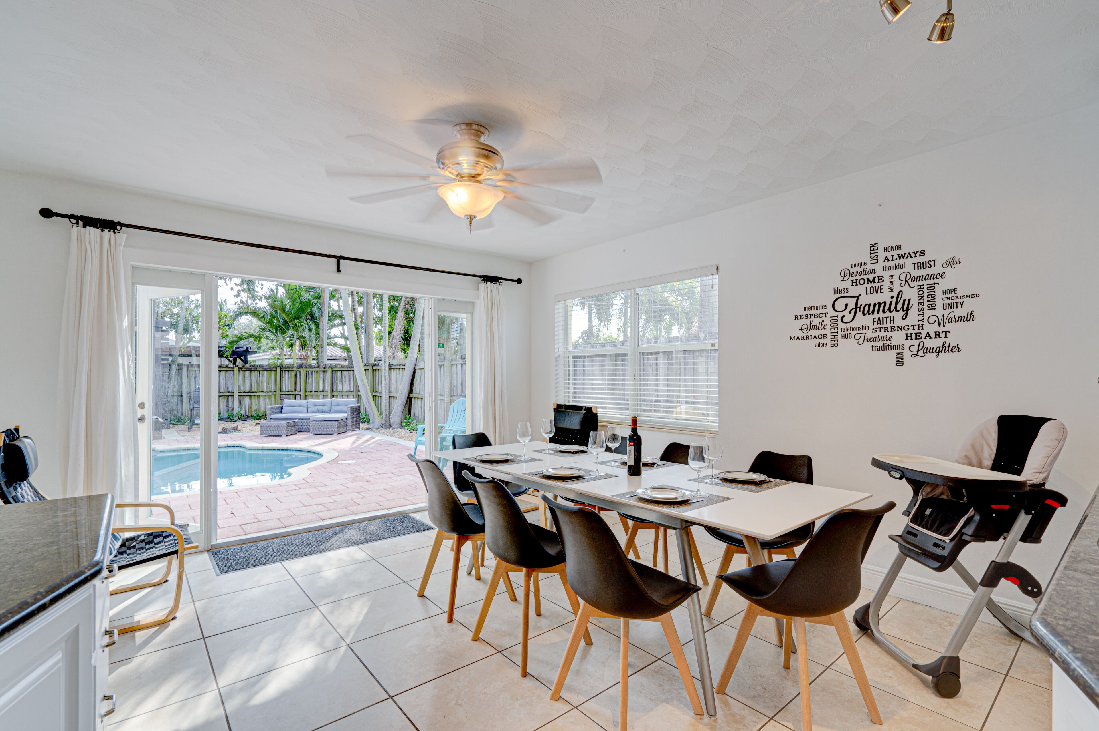 A dining area with a table set for four, chairs, a ceiling fan, and a view of a backyard with a pool.
