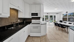 Eine moderne Küche mit weißen Schränken, einem eingebauten Backofen und einer Mikrowelle. Es gibt einen Essbereich mit Tisch und Stühlen.