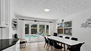 Eine moderne Küche mit Essbereich und Blick auf einen Pool, innen in Weiß gehalten.
