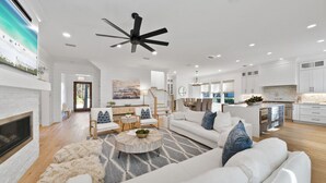 A spacious living room with a fireplace, white sofas, a round coffee table, and a ceiling fan. - Luxurious 4-BR Home w/ Private Pool & Beach Access – Golf Cart & Bikes Included (Santa Rosa Beach)
