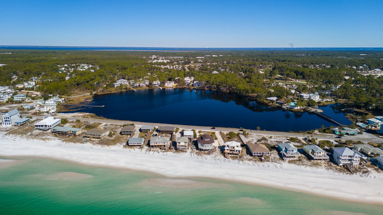 Luchtbeeld van een kustgebied met een groot wateroppervlak, strandwoningen en een combinatie van woon- en commerciële gebouwen.