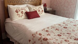 A neatly made bed with floral bedding, a wooden headboard, and a nightstand with a lamp. - AH #11 · AH #11 Queen Suite w/Tub/Shower (Wabasha)