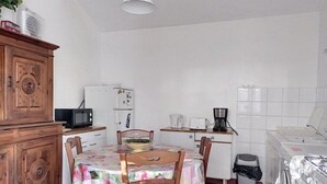 Een functionele keuken met een eettafel, stoelen, een koelkast, een magnetron, een koffiezetapparaat en een wasmachine.