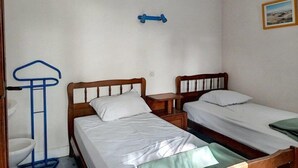 Een kleine, eenvoudige kamer met twee houten bedden, een enkele stoel en een tafeltje.