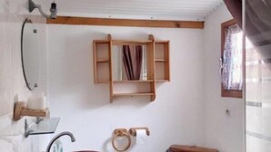 Een badkamer met een houten wastafelmeubel, twee toiletten, een spiegel en een raam met gordijnen.