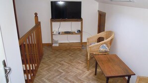 A room with a wooden floor, a television on a stand, a wicker chair, and a small table. - Ref 518 - Soulacaise near downtown (SOULAC SUR MER)
