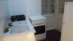 A small kitchen with white appliances, including a stove, oven, and sink. There are decorative tiles on the walls and a window with a sailboat pattern. - Ref 518 - Soulacaise near downtown (SOULAC SUR MER)