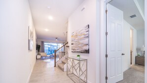 Un pasillo moderno con una mesa consola de vidrio, una escalera y una puerta que conduce a otra habitación.