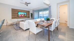 Un comedor moderno con una mesa de madera, sillas blancas y un televisor montado en la pared.