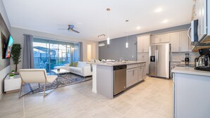 Una cocina moderna con una isla central, electrodomésticos de acero inoxidable y un comedor con un sofá blanco y una planta.