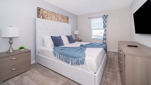 Un dormitorio moderno con una cama blanca, una mesita de noche con lámpara, un televisor y un armario de madera.