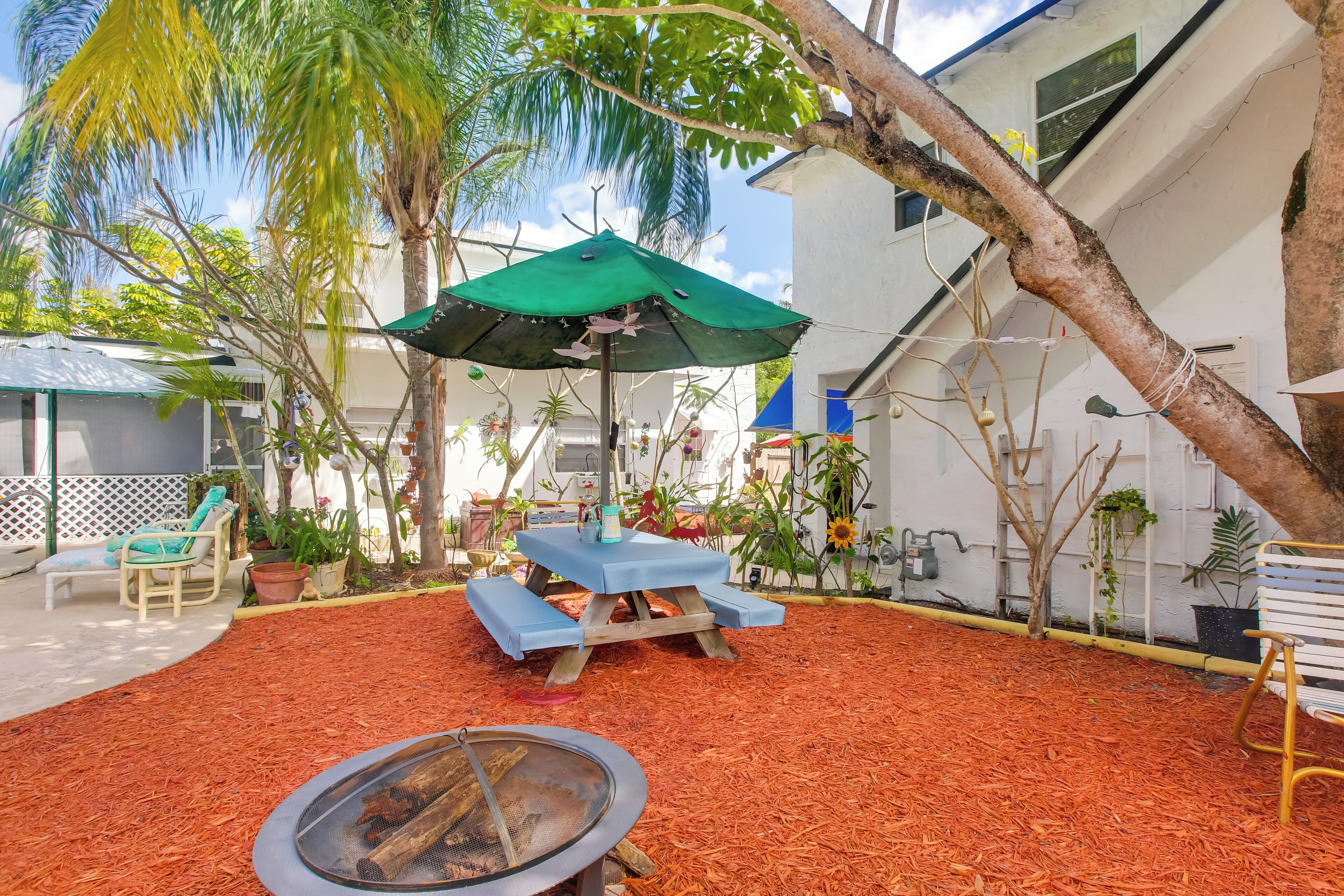 A patio area with a fire pit, a table with an umbrella, and various potted plants.