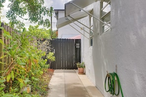 A narrow concrete pathway leading to a black gate, flanked by potted plants and a white wall.