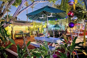 An outdoor patio area with a table and chairs, surrounded by plants and decorative lights.