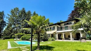 Ein zweistöckiges Haus mit Swimmingpool, umgeben von üppiger Vegetation und Palmen.
