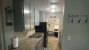 A kitchen with grey cabinets, a black refrigerator, and a wooden floor. There is a welcome sign on the wall. - 3.2 miles to the beaches and Bay, Cute Florida Cottage (Fort Walton Beach)