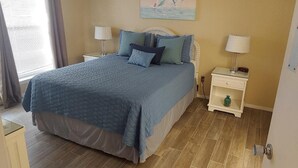 Ein Schlafzimmer mit einem Bett, zwei Nachttischen, einer Lampe, einem Gemälde und einem Fenster mit Vorhängen.