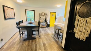 Un coin repas avec une table et des chaises en bois, une petite plante posée sur la table et une porte jaune en arrière-plan.