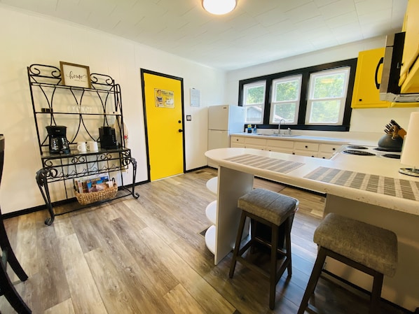 A compact kitchen with a central island, a coffee station, and a yellow door.