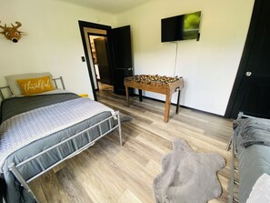 A bedroom with a bed, a foosball table, a television, and a door leading to another room.