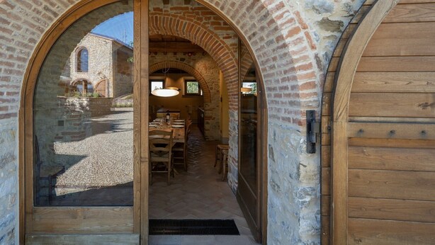 Un'imponente ingresso ad arco in pietra conduce a una sala da pranzo con un tavolo apparecchiato per due, una porta in legno sulla destra e un edificio in pietra sullo sfondo.