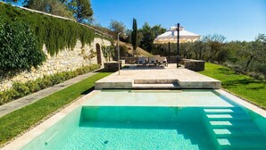 Una piscina con acqua cristallina, un muro in pietra e un'area relax con ombrelloni.