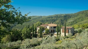 Una rustica casa in pietra con tetto in tegole, immersa tra uliveti e cipressi, con vista su dolci colline.