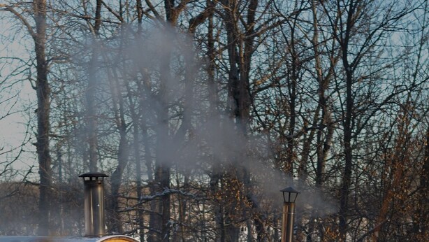 Banyera de fusta enclavada en una zona boscosa, amb neu al voltant i vapor que s'aixeca.