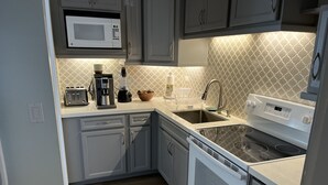 Una cocina moderna con armarios grises, un microondas, una cafetera, una licuadora, un fregadero y una estufa.