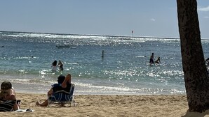 Escena de playa con gente descansando en la arena y nadando en el agua.