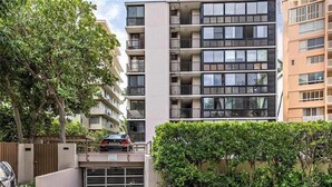 Un edificio residencial de varios pisos con balcones, zona de estacionamiento protegida por una reja y una siega bien cuidada.