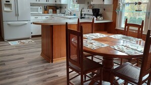 Une cuisine avec des meubles de rangement en bois, un réfrigérateur blanc, une table à manger avec des chaises et un ventilateur de plafond.
