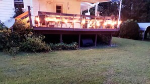 Une terrasse dotée d’un éclairage extérieur, entourée de pelouse et d’arbustes.