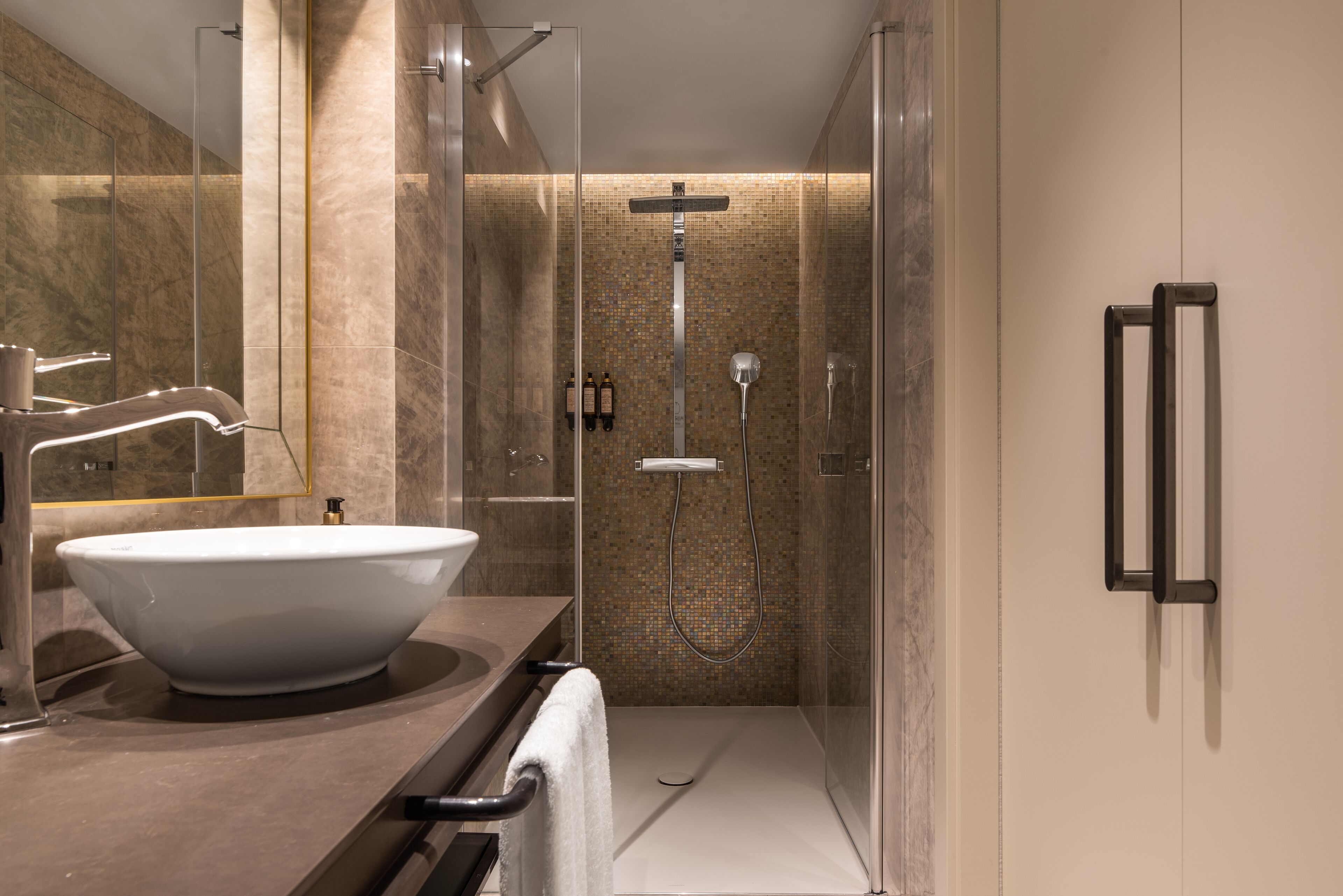 A modern bathroom with a large white sink, a glass shower enclosure, and a marble-tiled wall.