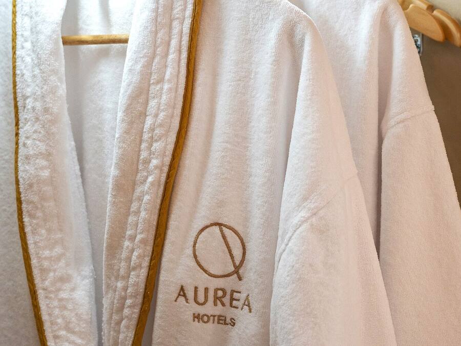 Una bata blanca con ribete dorado y el texto 'AUREA HOTELS' bordado.
